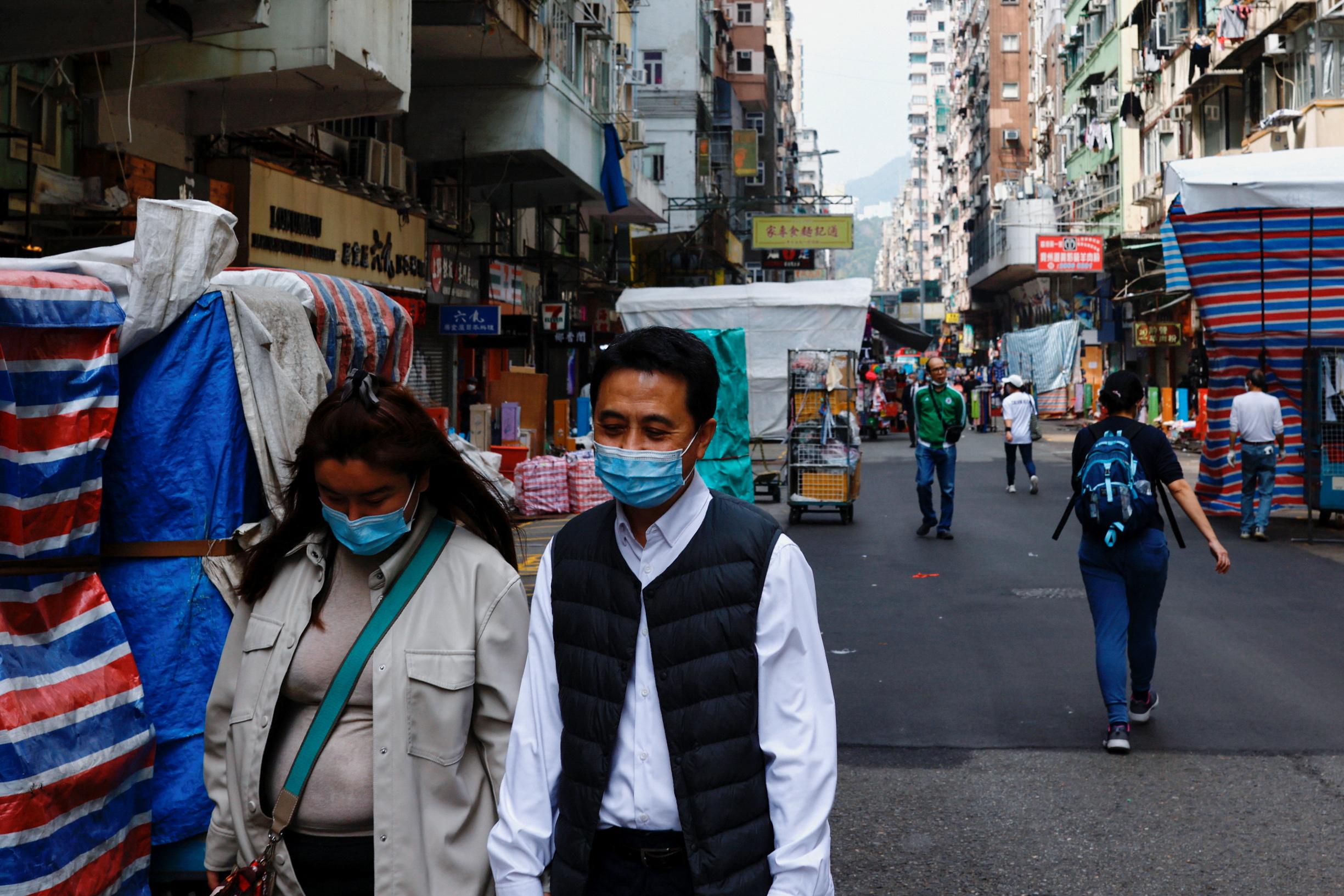 Two people wearing face masks walk down a street.